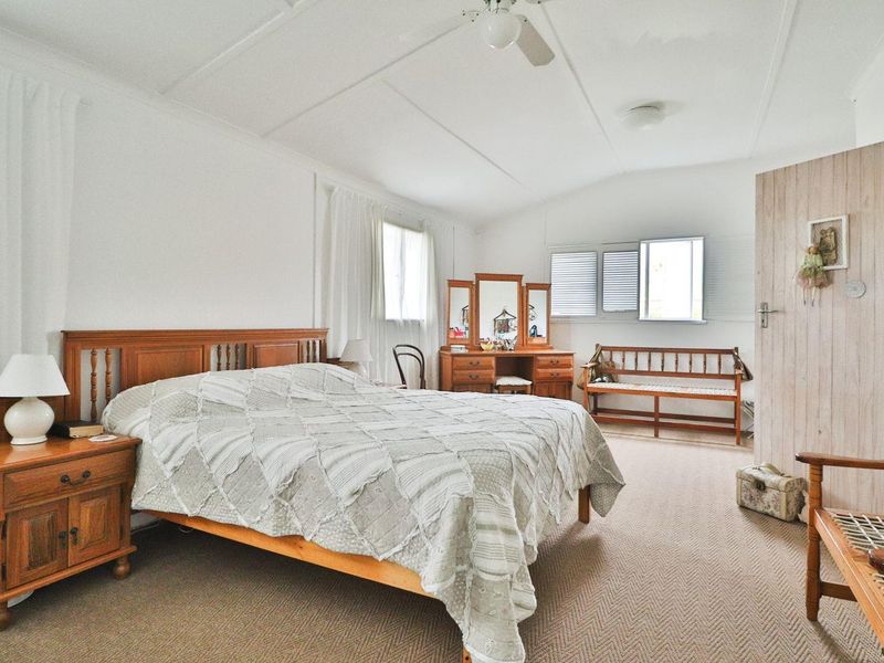 A spacious bedroom featuring neutral carpeted flooring, a ceiling fan, and classic casement windows, offering a comfortable and functional living space.