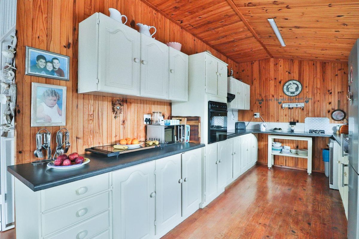 A rustic kitchen featuring timber wall and ceiling cladding, white built-in cabinetry, and dark laminate countertops with a built-in oven.