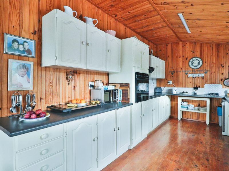 A rustic kitchen featuring timber wall and ceiling cladding, white built-in cabinetry, and dark laminate countertops with a built-in oven.