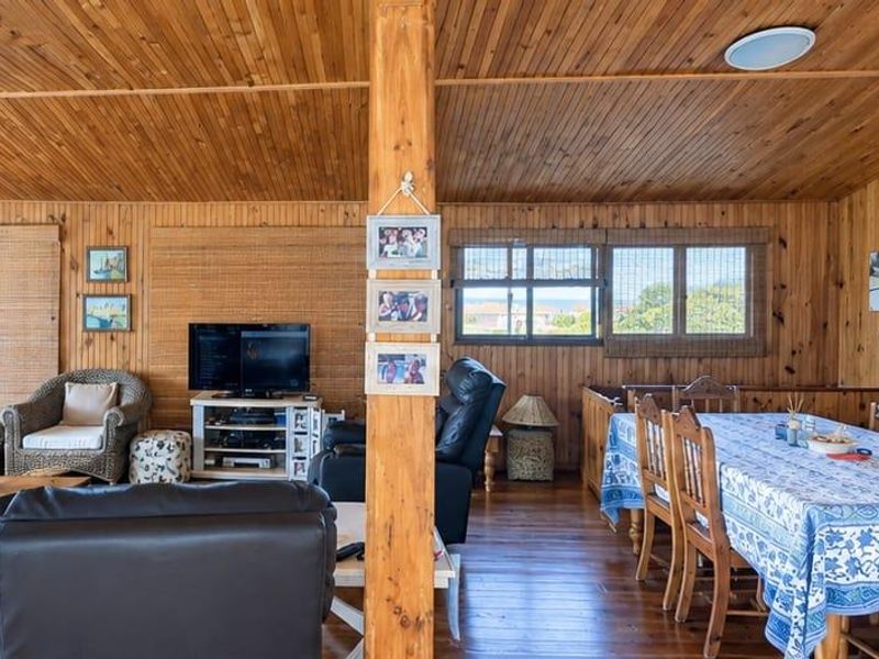 Open-plan living and dining area featuring extensive timber wall and ceiling cladding, hardwood flooring, and a freestanding fireplace.