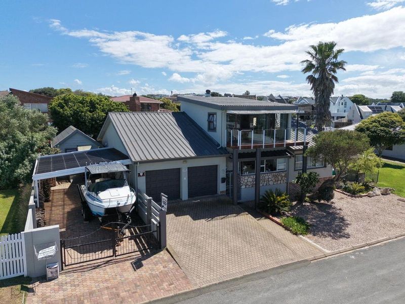Aerial view of a residential property featuring a double garage, paved driveway, carport, and an upper-level balcony with glass railings.