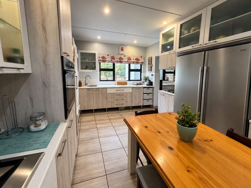 A well-maintained kitchen featuring light wood-tone cabinetry, tiled flooring, integrated appliances, and ample storage space with glass-fronted upper cabinets.