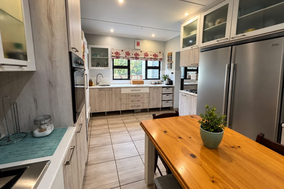 A well-maintained kitchen featuring light wood-tone cabinetry, tiled flooring, integrated appliances, and ample storage space with glass-fronted upper cabinets.