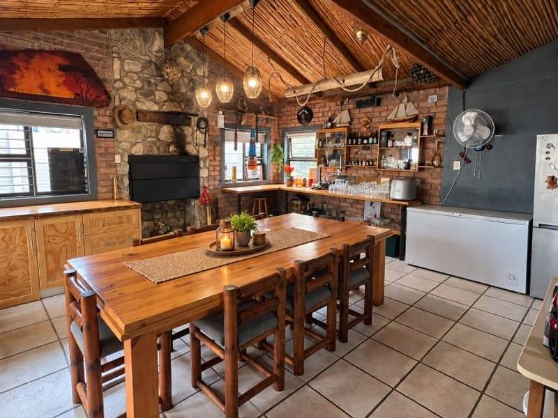 Spacious open-plan living and dining area featuring a rustic stone fireplace, exposed timber ceiling beams, and built-in cabinetry with tiled flooring throughout.