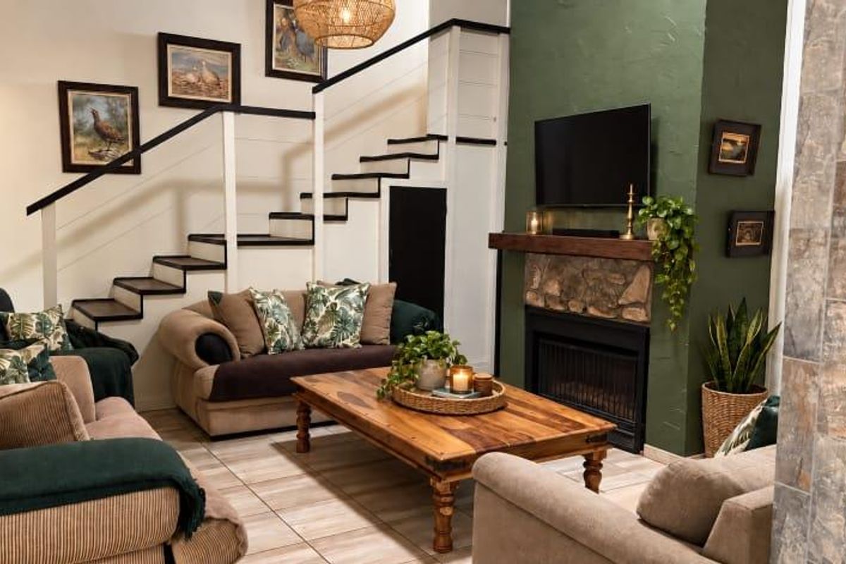 Cozy living room featuring a stone fireplace with a wooden mantelpiece, tiled flooring, and an integrated staircase.