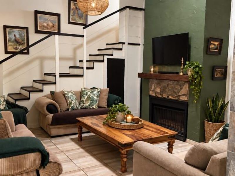 Cozy living room featuring a stone fireplace with a wooden mantelpiece, tiled flooring, and an integrated staircase.