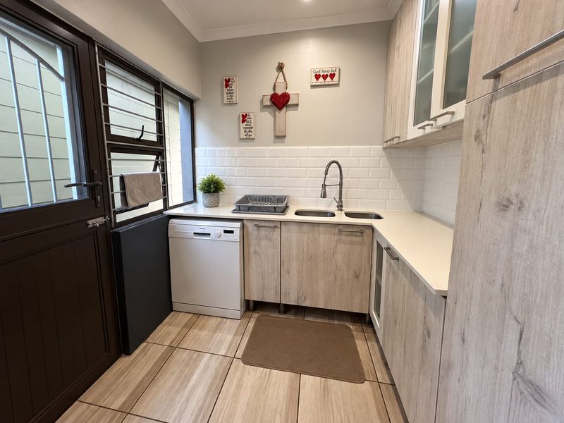 A well-maintained laundry area featuring light wood-grain cabinetry, subway tile backsplash, double basin sink, and integrated dishwasher with direct exterior access.
