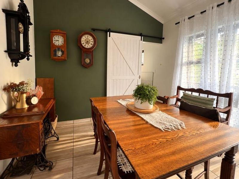 A well-maintained dining room featuring a vaulted ceiling, tiled flooring, and a distinctive white sliding barn door against a dark green accent wall.