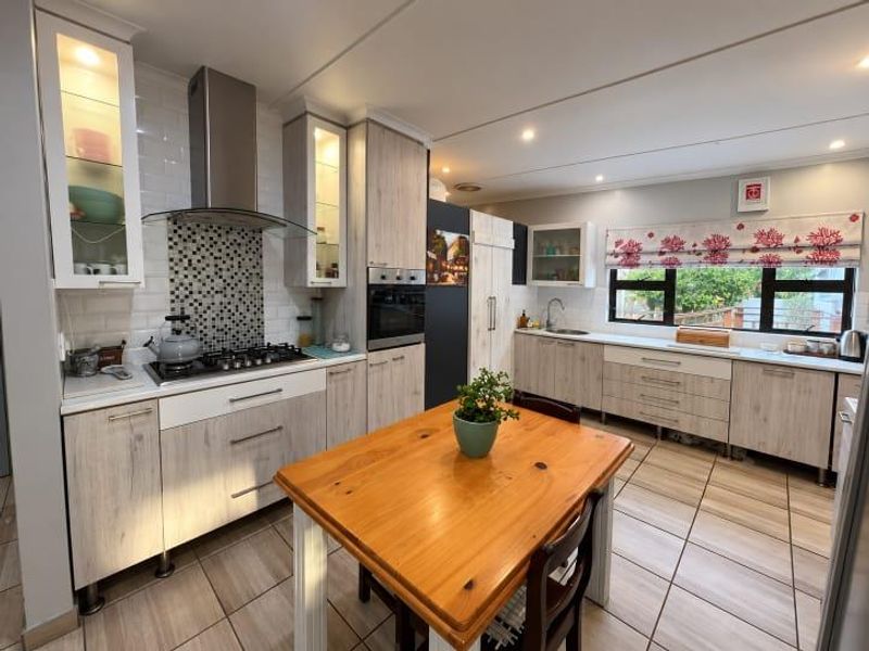 A well-maintained kitchen featuring light wood-grain cabinetry, a gas hob with extractor, subway tile backsplash, and tiled flooring throughout.