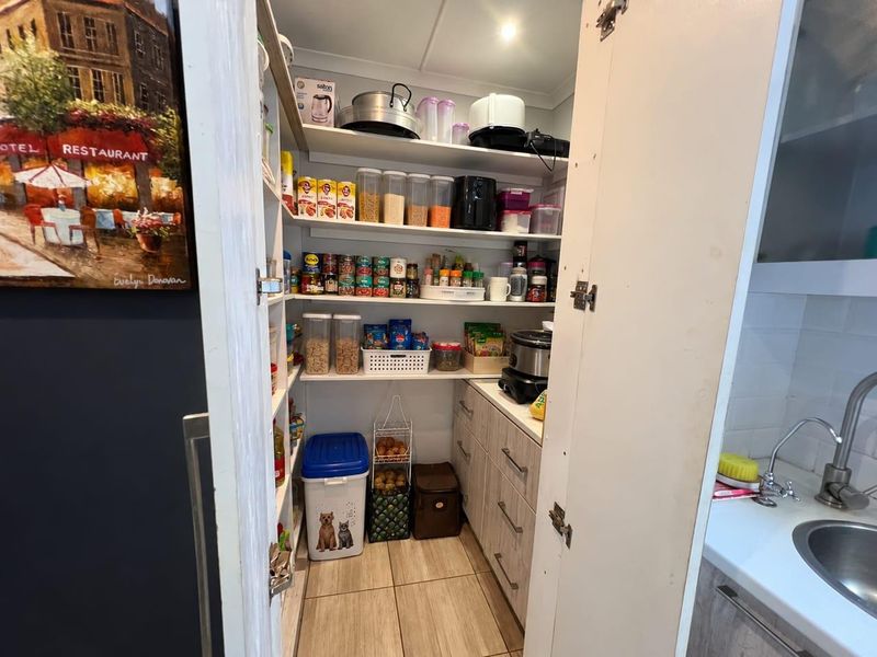 A functional scullery or pantry area featuring built-in shelving, laminate cabinetry, and a small sink, providing convenient additional storage and prep space.