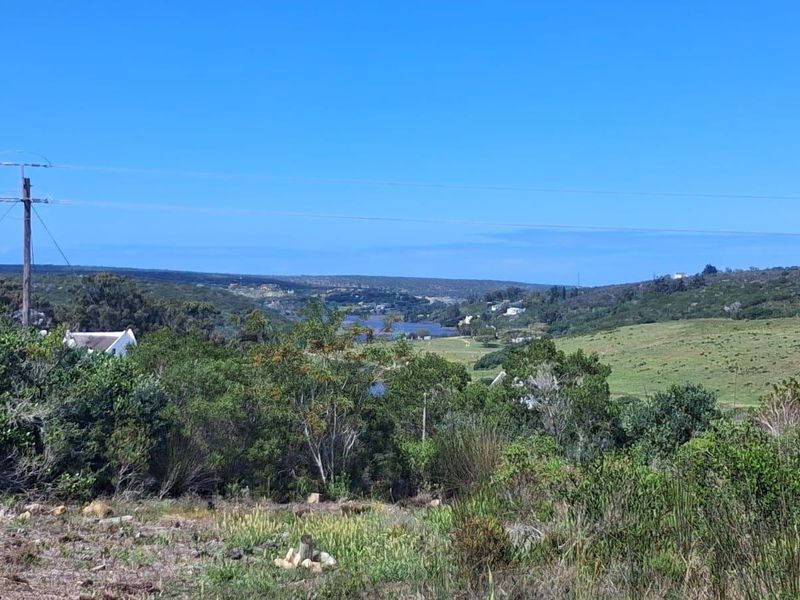 A scenic landscape view overlooking rolling hills, natural vegetation, and a distant water body from the vacant residential property.