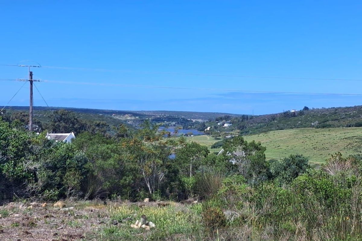 A scenic landscape view overlooking rolling hills, natural vegetation, and a distant water body from the vacant residential property.
