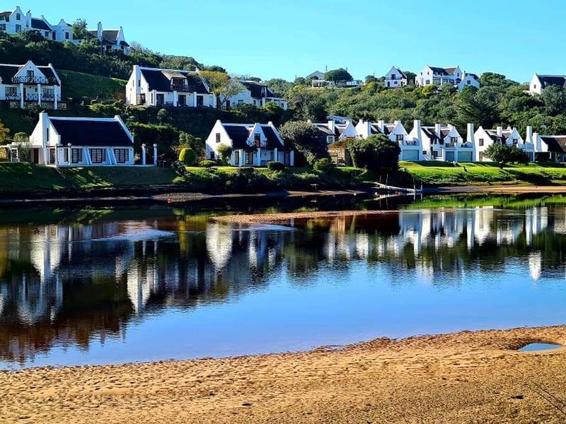 A scenic view of a residential estate situated along a tranquil riverbank, showcasing the surrounding coastal landscape and waterfront setting.