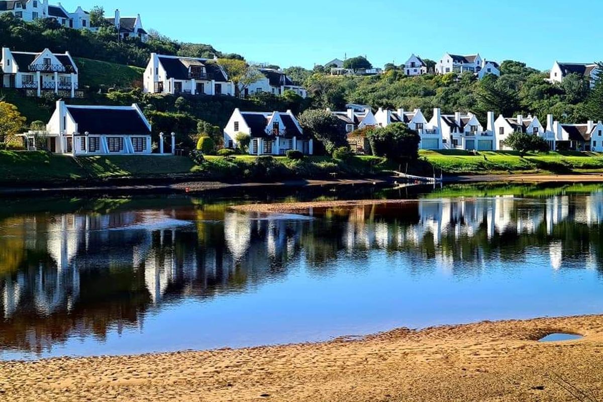 A scenic view of a residential estate situated along a tranquil riverbank, showcasing the surrounding coastal landscape and waterfront setting.