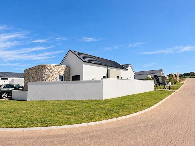 Modern residential property featuring stone cladding, a sleek metal roof, and a clean white boundary wall, situated in a well-maintained estate.