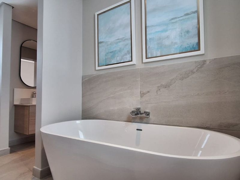 Modern bathroom featuring a sleek freestanding bathtub, stone-look wall tiles, and a floating vanity with a vessel sink.