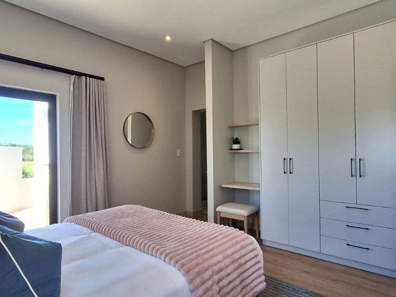 Modern bedroom featuring extensive built-in cabinetry, a built-in vanity area, laminate flooring, and a sliding glass door providing natural light.