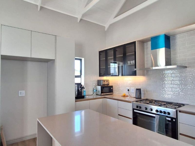 Modern kitchen featuring quartz countertops, subway tile backsplash, gas hob, built-in oven, extractor fan, and a central island under a vaulted ceiling.