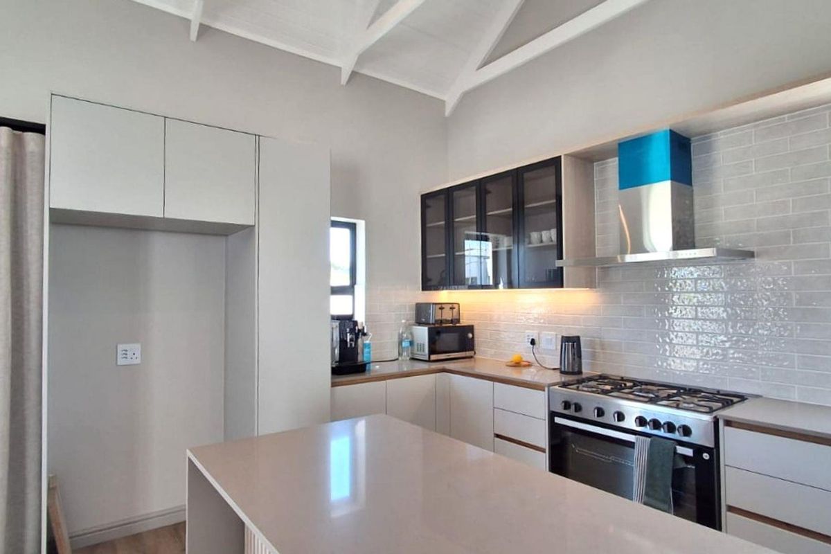 Modern kitchen featuring quartz countertops, subway tile backsplash, gas hob, built-in oven, extractor fan, and a central island under a vaulted ceiling.