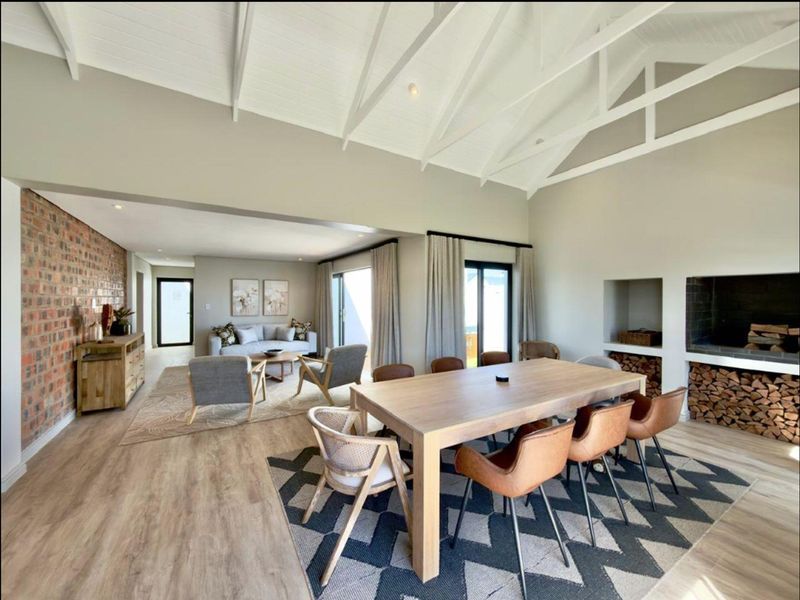 Spacious open-plan living and dining area featuring a vaulted ceiling with exposed beams, a built-in fireplace, and large sliding doors leading to the outdoors.