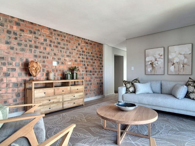 A well-presented living room featuring a prominent exposed brick feature wall and modern recessed downlighting, creating a warm and inviting atmosphere.
