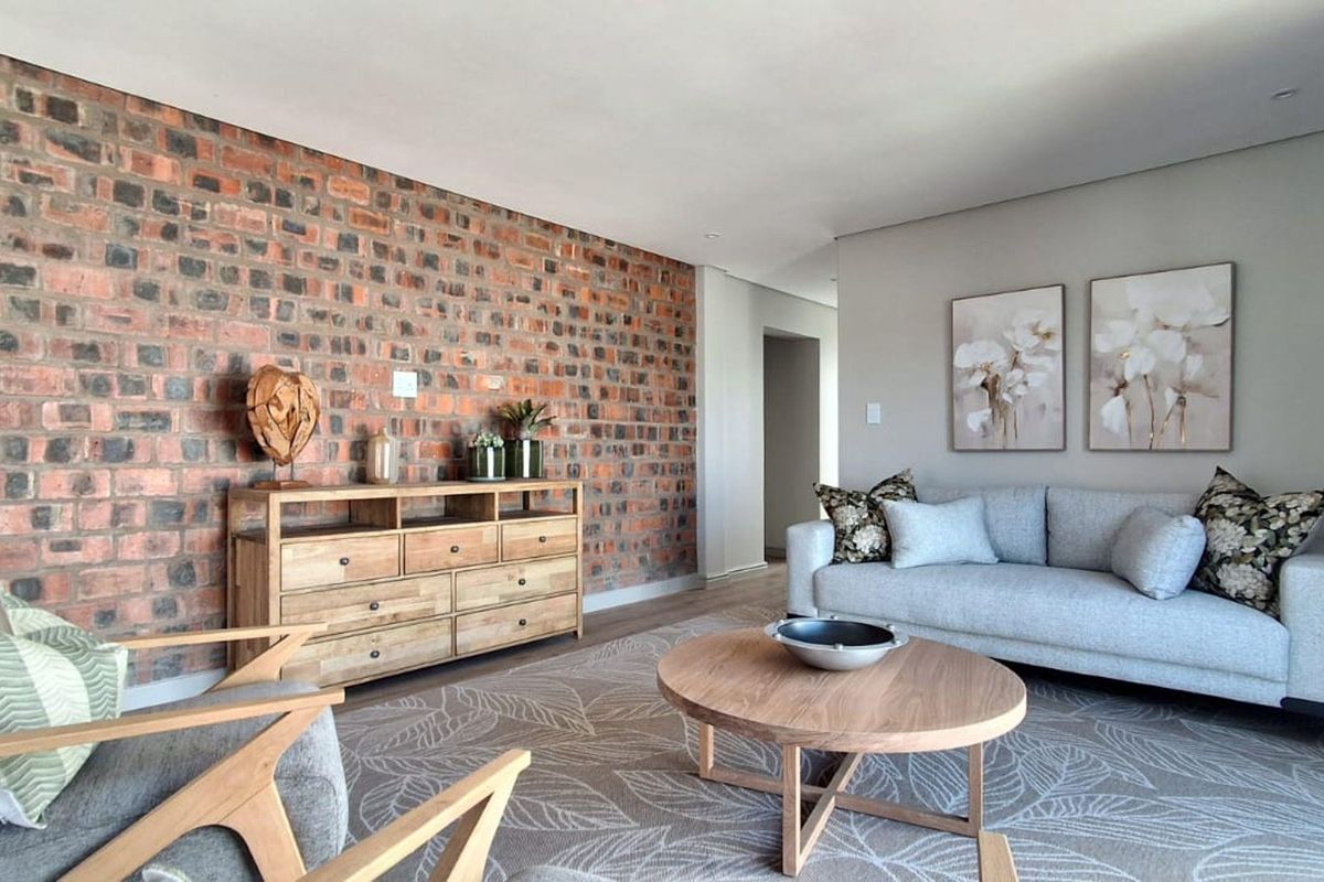A well-presented living room featuring a prominent exposed brick feature wall and modern recessed downlighting, creating a warm and inviting atmosphere.