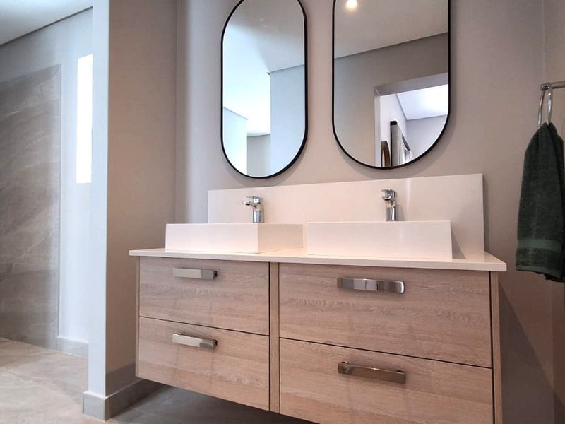 Modern bathroom featuring a double vanity with vessel sinks, wall-mounted mirrors, and a spacious walk-in shower with neutral tiling.