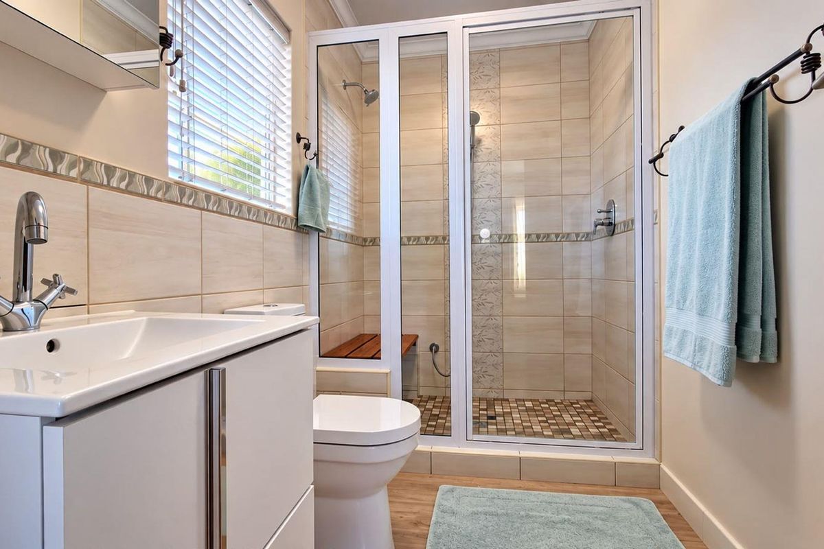 A well-maintained bathroom featuring a modern vanity, a glass-enclosed shower with tiled accents, and neutral wall tiling.