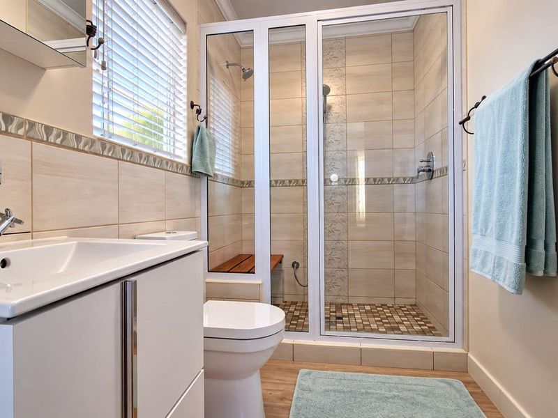 A well-maintained bathroom featuring a modern vanity, a glass-enclosed shower with tiled accents, and neutral wall tiling.