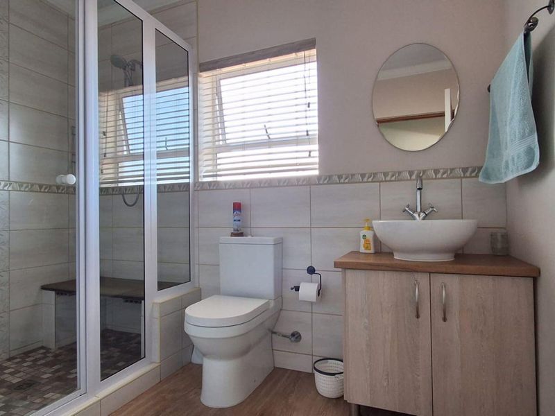 A well-maintained bathroom featuring a glass-enclosed shower with a built-in bench, a modern vessel sink on a vanity cabinet, and neutral wall tiling.