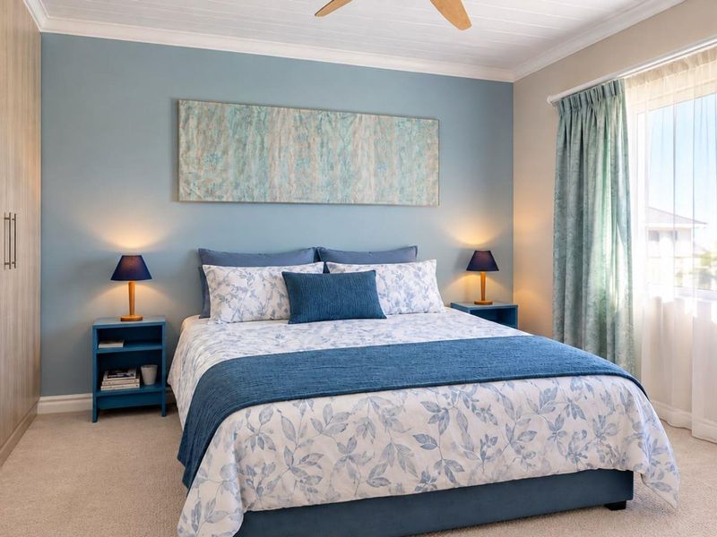 A well-maintained bedroom featuring a built-in wardrobe, ceiling fan, and neutral carpeting, finished with a soft blue accent wall.