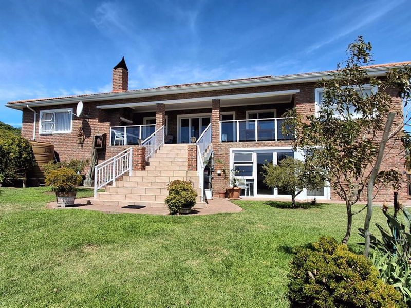 Rear view of a brick house featuring a raised patio with a tiled staircase, glass balustrades, and a spacious garden with water storage tanks.