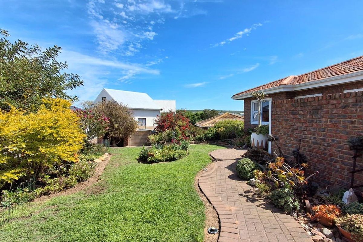 A well-maintained rear garden featuring a brick-paved pathway, established landscaping, and a classic brick exterior facade under a tiled roof.