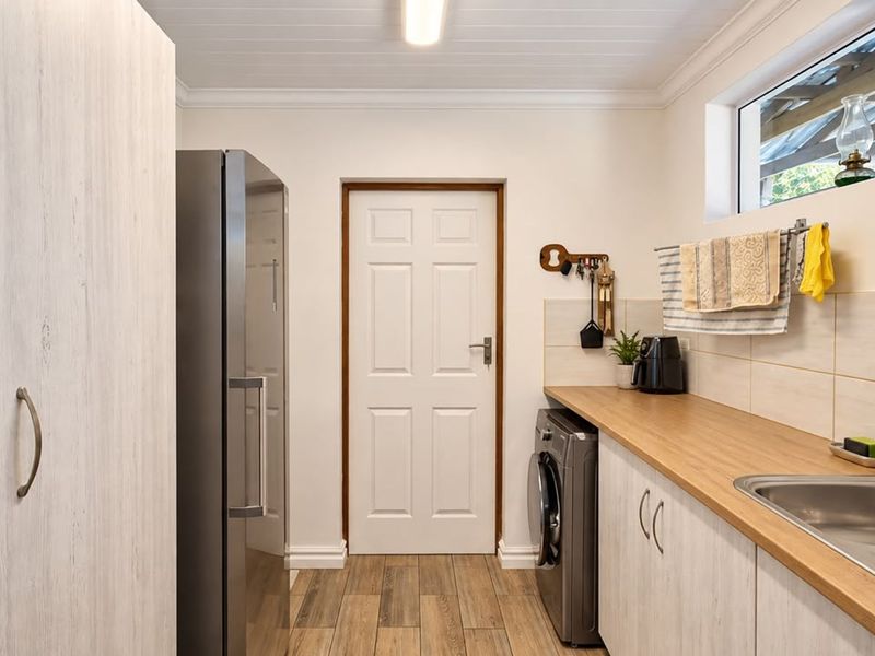 A well-maintained laundry room featuring built-in cabinetry, a laminate countertop, stainless steel sink, and durable timber-look flooring.