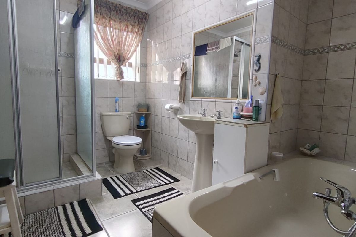 A functional bathroom featuring a shower enclosure, bathtub, pedestal basin with vanity storage, and neutral ceramic wall and floor tiling.