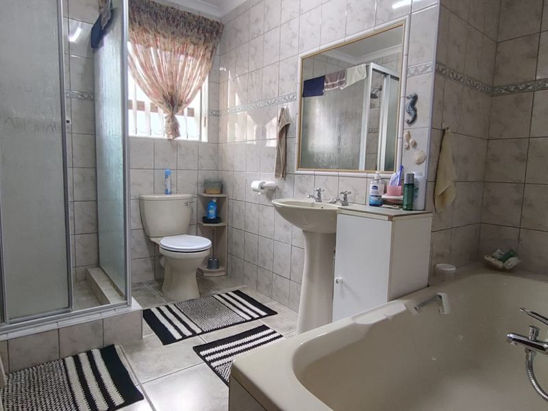 A functional bathroom featuring a shower enclosure, bathtub, pedestal basin with vanity storage, and neutral ceramic wall and floor tiling.
