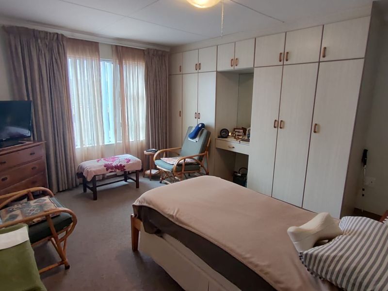 A spacious bedroom featuring extensive built-in cupboards with an integrated vanity unit and large windows allowing for natural light.
