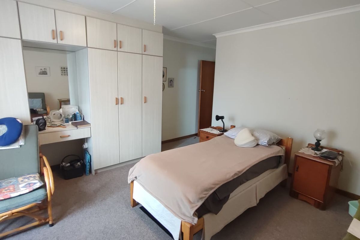 A functional bedroom featuring extensive built-in cabinetry with an integrated vanity unit, neutral wall finishes, and carpeted flooring.
