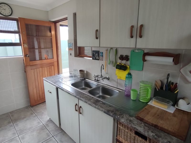 A functional scullery area featuring double stainless steel sinks, laminate countertops, ample built-in cabinetry, and tiled flooring with direct access to the exterior.