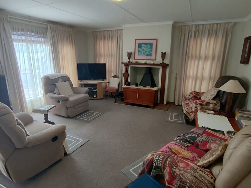 A spacious living room featuring a central fireplace with a wooden mantelpiece and large windows dressed with curtains.