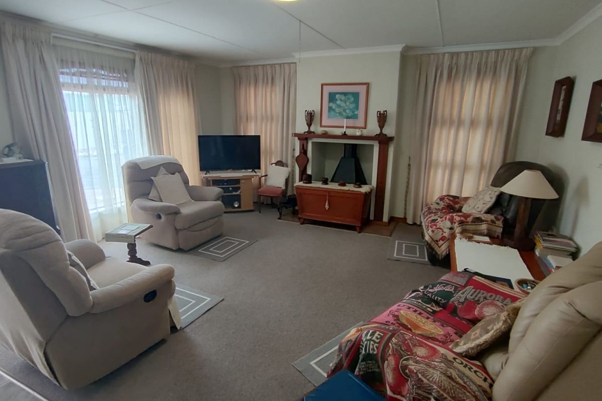 A spacious living room featuring a central fireplace with a wooden mantelpiece and large windows dressed with curtains.