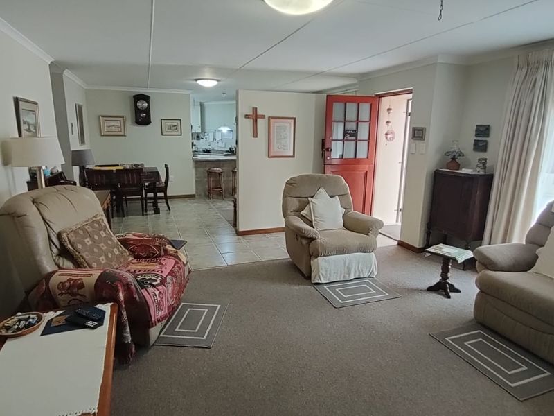Open plan living area featuring a carpeted lounge space transitioning into a tiled kitchen area with a partial dividing wall and exterior access.
