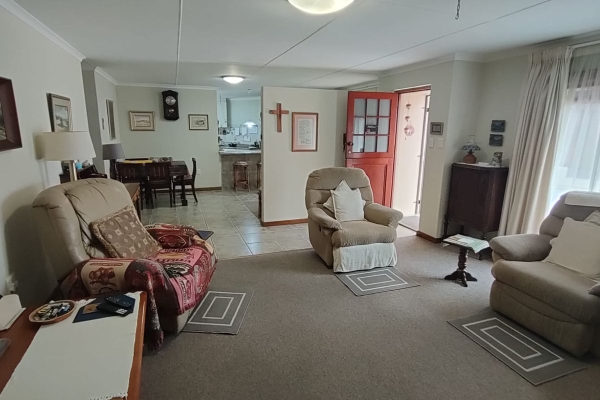 Open plan living area featuring a carpeted lounge space transitioning into a tiled kitchen area with a partial dividing wall and exterior access.