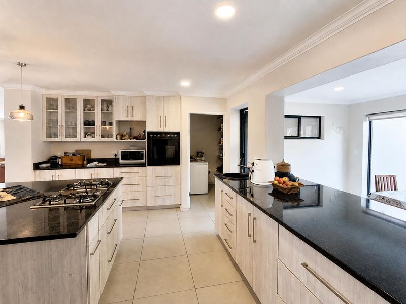 Modern kitchen featuring light wood-grain cabinetry, dark granite countertops, a central island with a gas hob, and a separate scullery area.