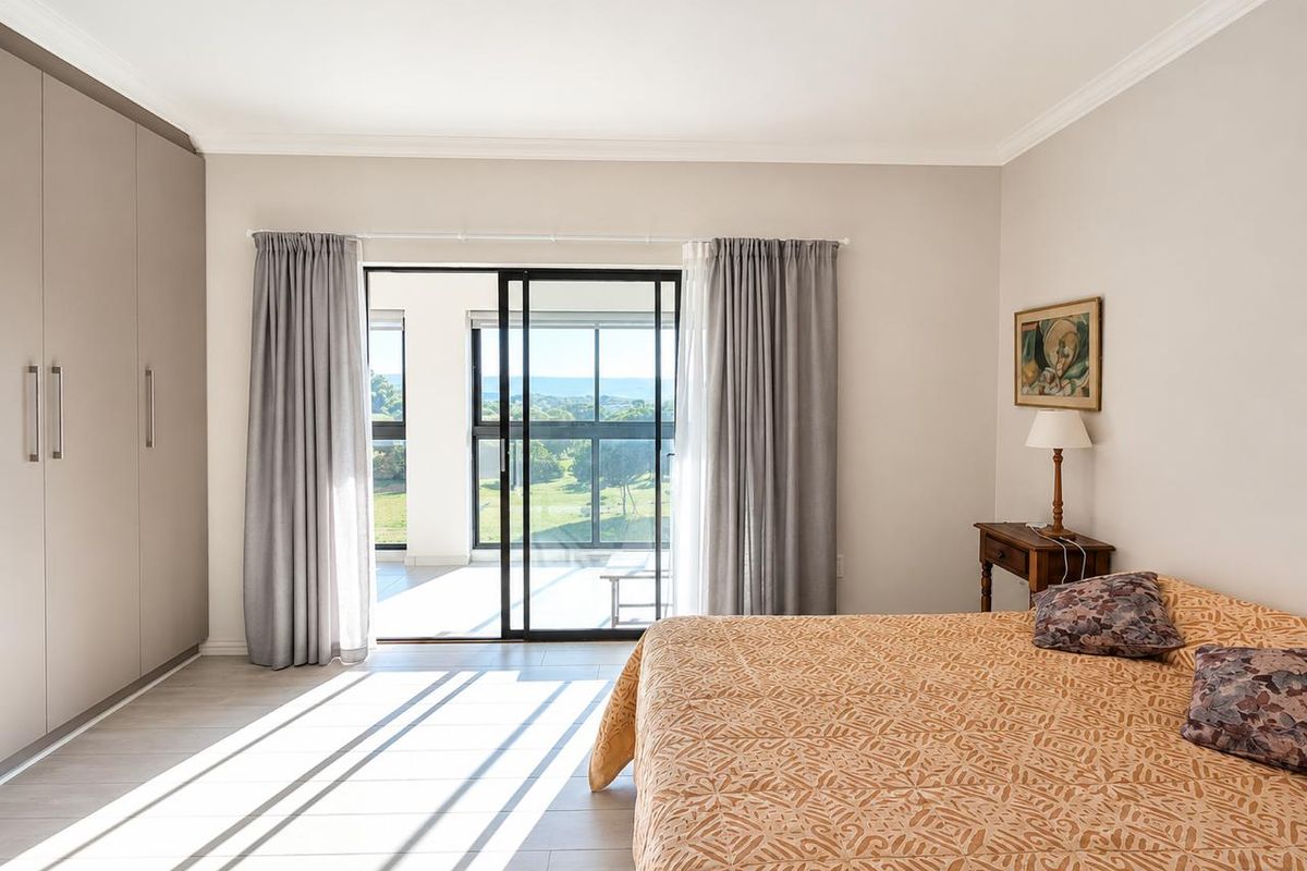 Spacious bedroom featuring built-in cupboards, modern laminate flooring, and a sliding glass door providing access to a balcony with scenic views.