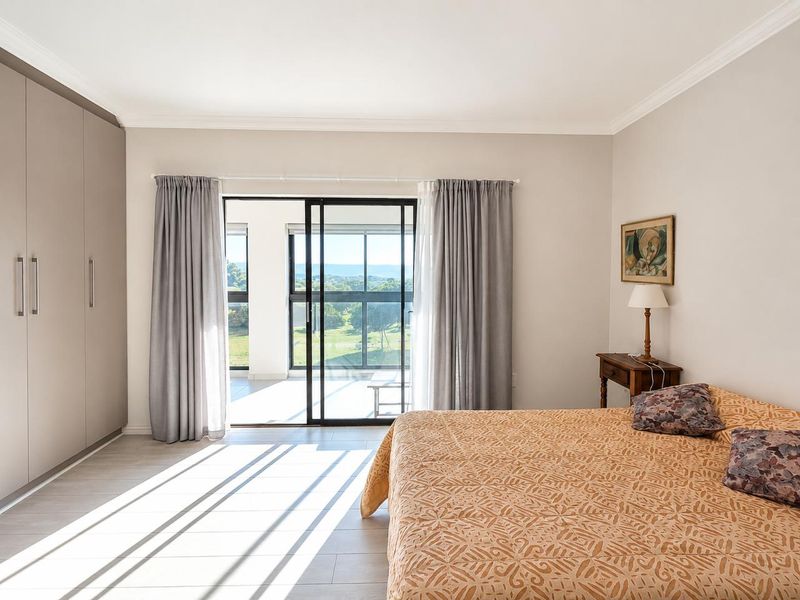 Spacious bedroom featuring built-in cupboards, modern laminate flooring, and a sliding glass door providing access to a balcony with scenic views.
