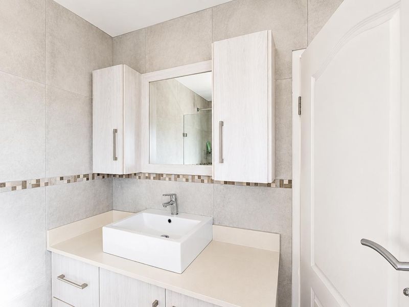 A modern bathroom featuring a vessel sink, vanity cabinet with integrated mirror and storage, and neutral wall tiling with a decorative mosaic border.