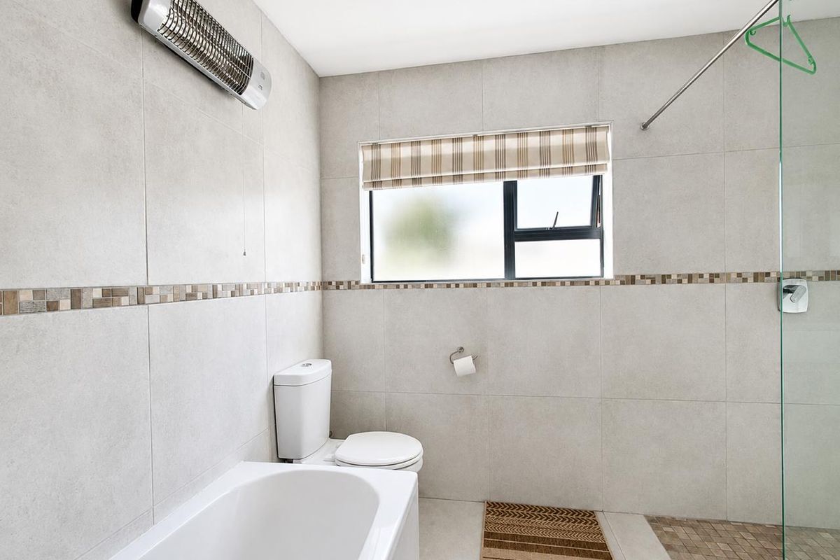 A clean, modern bathroom featuring neutral wall tiles, a built-in bathtub, a separate shower area with a glass screen, and a wall-mounted heater.