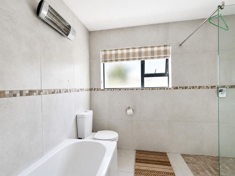A clean, modern bathroom featuring neutral wall tiles, a built-in bathtub, a separate shower area with a glass screen, and a wall-mounted heater.