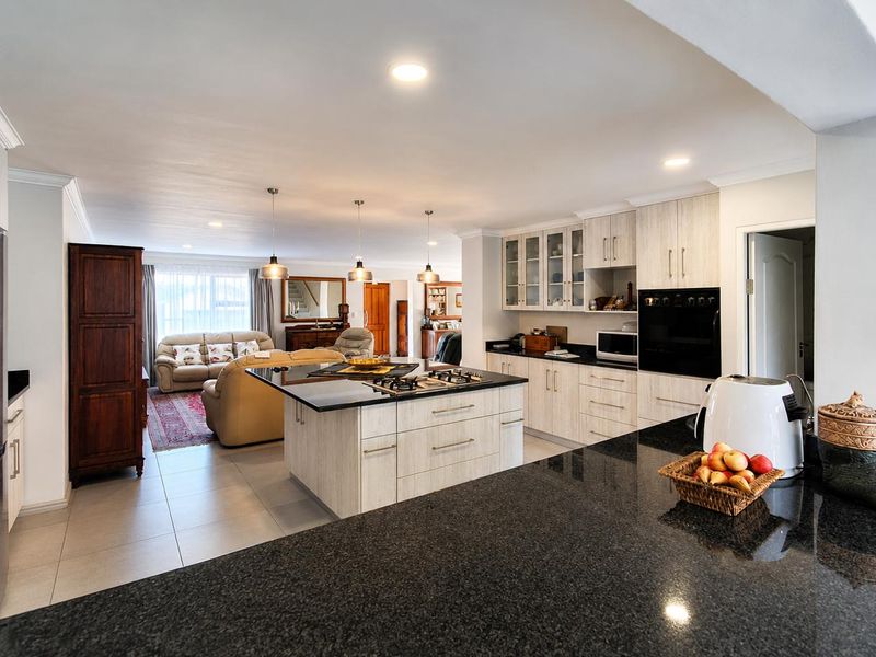 Spacious open-plan kitchen and living area featuring a central island with granite countertops, built-in oven, gas hob, and modern cabinetry.